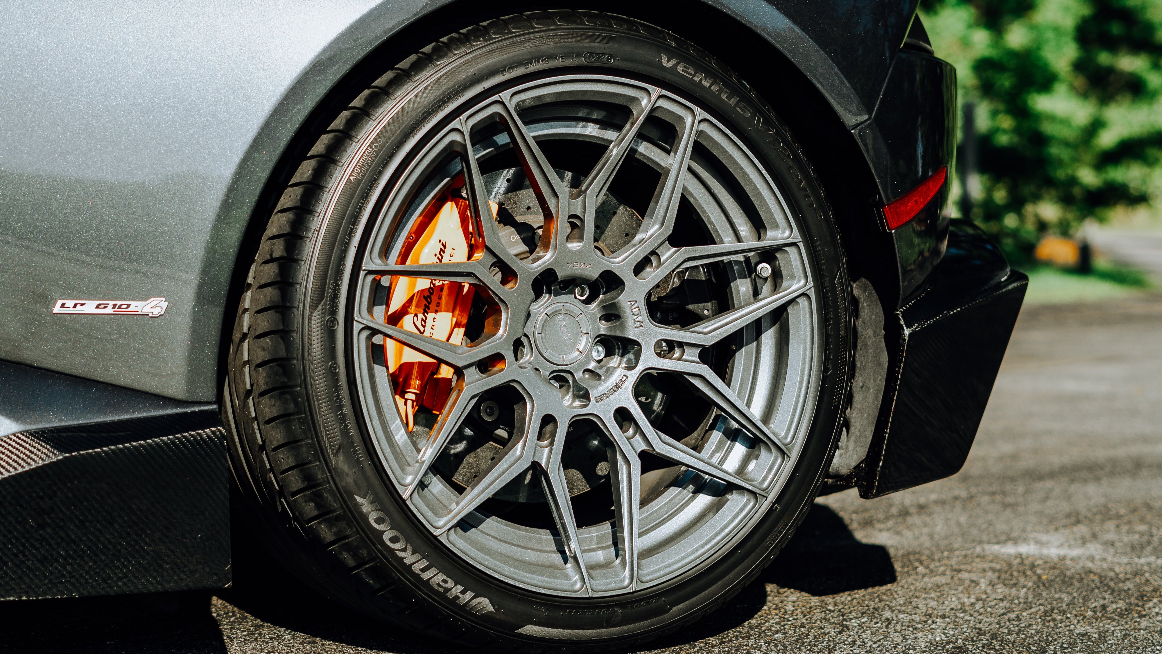 Close-up of a car wheel with a detailed rim on a road with trees in the background